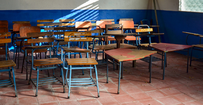 foto de uma sala de aula vazia, com cadeiras bagunçadas e encostadas no canto da sala.